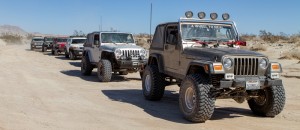A Line of Jeeps follow a champaign colored 2 door TJ with a 4 Wheel to Heal windsheild sticker 
