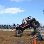 A heavily modified Jeep Wrangler buggy is just about to bring it's back tires off a large rock after completing a rock obstacle course
