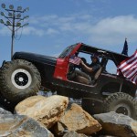 A Jeep Wrangler with American Flags flying in the back crawls over large rocks